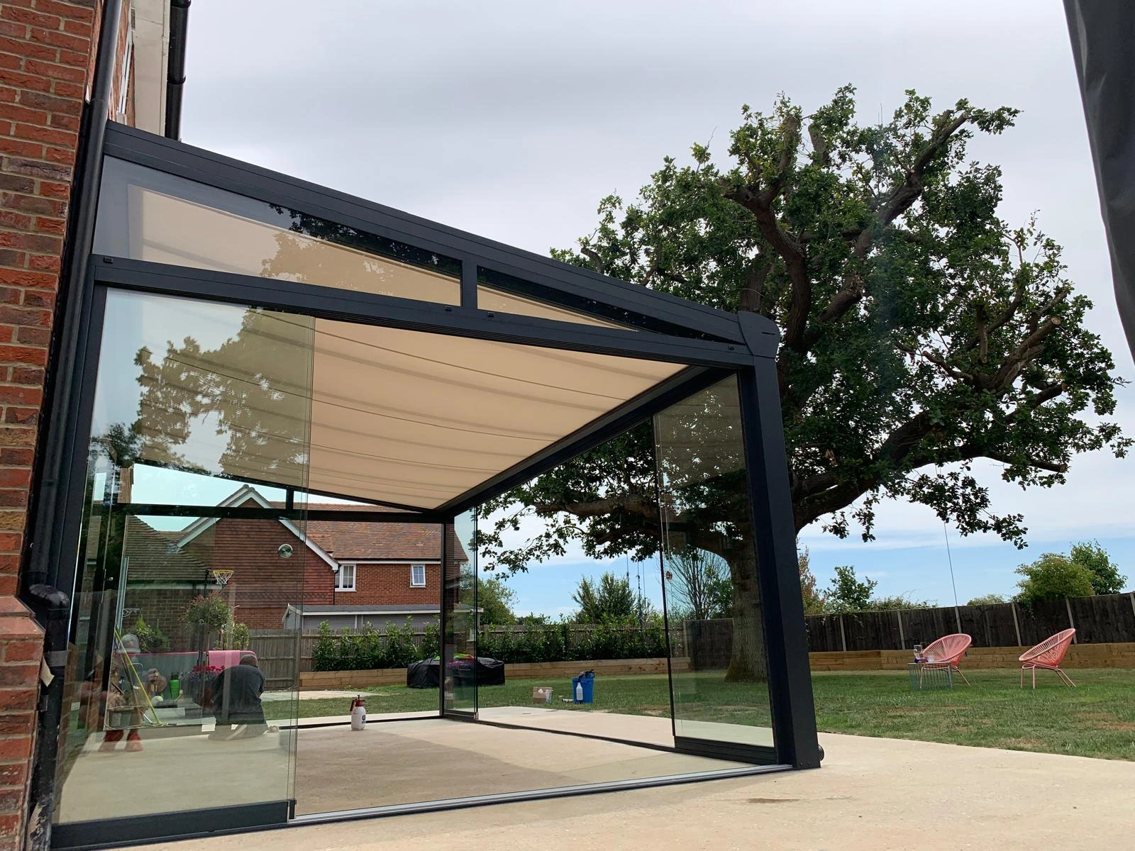 Anthracite grey aluminium framed glass room veranda with opened sliding doors and a fully extended beige roof awning.